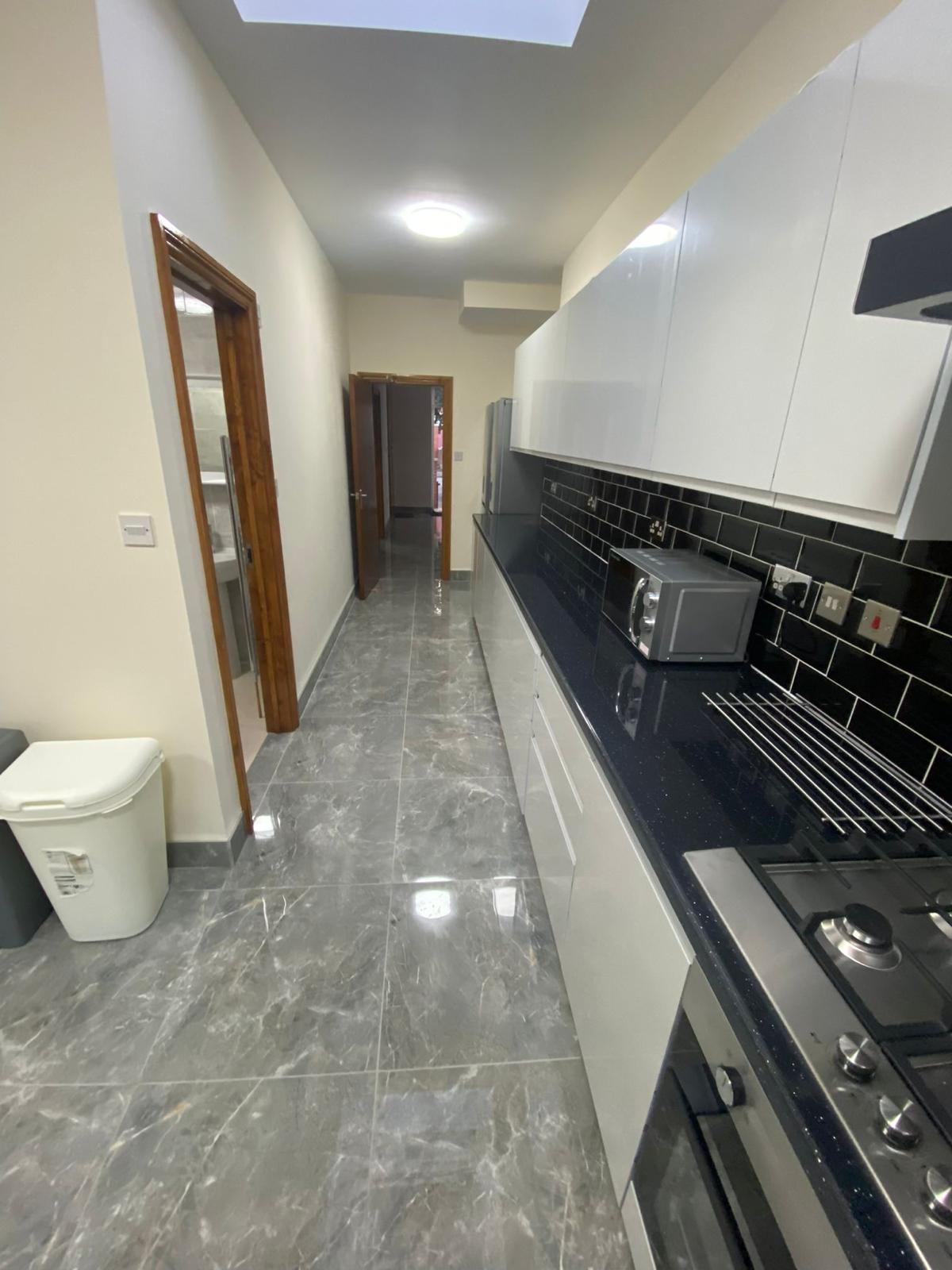 Galley kitchen with white gloss units, black splashback and skylight
